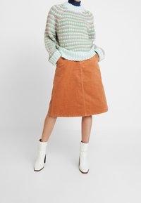 Jersey de punto con rayas en tonos pastel de rosa y verde, combinado con una falda corta de pana marrón en corte A y botas blancas de tobillo con tacón cuadrado.