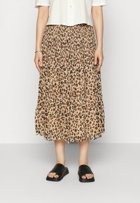 Falda midi plizada en beige con un estampado de leopardo. Combinada con sandalias negras tipo slide. La tela tiene una textura suave y fluida.