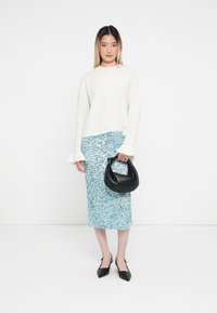 Weißer gestrickter Pullover, hellblauer Paillettenrock, schwarze Handtasche, spitze schwarze High Heels. Sanfte Texturen, entspannte Passform und klare Linien.