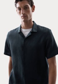 Camisa de manga corta verde oscuro en corte relajado, fabricada con tejido texturizado, con cuello tipo spread y cierre de botones oculto.