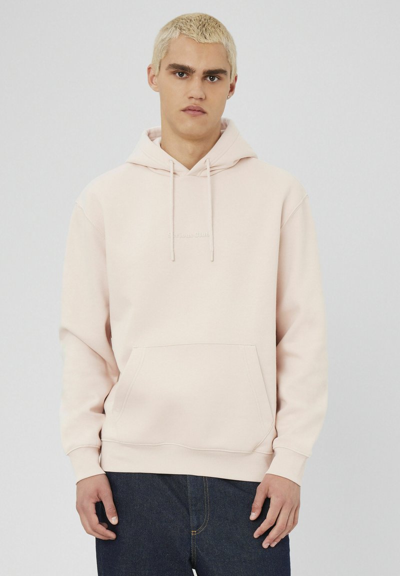 Hoodie rose clair en tissu doux avec une poche frontale et une capuche à cordon de serrage. Doté d'un logo brodé minimaliste sur la poitrine.