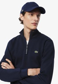 Marineblauwe halfrits sweatshirt met een zachte textuur, voorzien van een groene geborduurde krokodillenlogo op de borst. Vergezeld van een bijpassende pet.