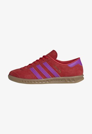 Baskets basses en daim rouge Adidas avec des bandes violettes, semelle en gomme et inscription « Hamburg » en lettres dorées sur le côté.