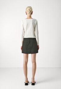 Chemise à manches longues légère et jupe en denim vert foncé. La jupe présente une coupe droite avec des coutures visibles et une fermeture éclair à l'arrière.