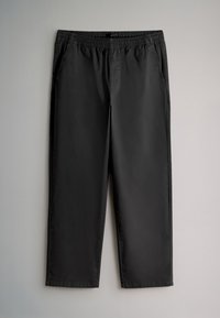Pantalon noir à taille élastique avec poches latérales, coupe droite et ourlets cousus, posé à plat sur un fond gris clair.