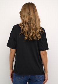 T-shirt nera a maniche corte con vestibilità rilassata, morbido materiale in cotone e scollo tondo. Indossata con jeans in denim blu.