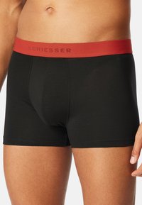 Czarne bawełniane bokserki z czerwonym elastycznym paskiem w talii, na którym nadrukowano markę "SCHIESSER" w ciemnoczerwonym kolorze. Gładka tekstura, dopasowany krój.