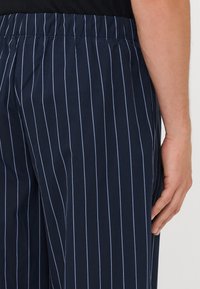 Marineblauwe gestreepte broek met een elastische tailleband, lichte stof en dunne lichtblauwe verticale strepen voor extra textuur.