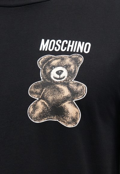 Μαύρο φούτερ με σχέδιο αρκούδας σε μπεζ χρώμα με λεπτομέρειες και τη λέξη "MOSCHINO" σε λευκό πάνω από την εικόνα.