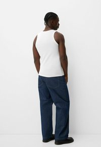 Vit ärmlös topp som kombineras med mörkblå vida jeans. Jeansen har en klassisk femfickorsdesign och synliga sömnadsdetaljer.