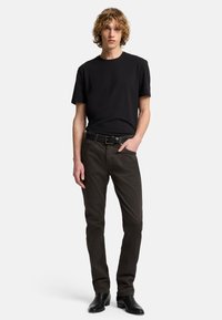 Schwarzes Baumwoll-T-Shirt mit kurzen Ärmeln, kombiniert mit dunkelbordeauxfarbigen Slim-Fit-Hosen und schwarzen Leder-Stiefeletten. Schlichte, glatte Texturen.
