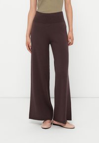 Femme portant un pantalon en maille pour femme taille haute et à jambes larges de couleur violet foncé et des ballerines beiges sur fond blanc.