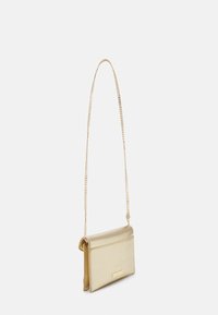 Sac bandoulière en métal doré avec une chaîne, de forme rectangulaire, texture lisse, et fermeture à rabat avec un petit logo en accent.
