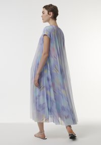 Vestido largo y fluido de tela transparente en tono púrpura pastel con pleats. Presenta patrones de color abstractos y suaves, y mangas cortas. Diseño minimalista.
