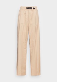 Beżowe spodnie o szerokich nogawkach, wykonane z gładkiego materiału, z elastycznym pasem w czarną klamrę i plisowanym przodem.