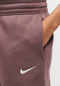 Φόρμες Nike σε σκονισμένο μοβ χρώμα, με ριμπ λάστιχο στη μέση, πλαϊνή τσέπη και λευκό λογότυπο στο πόδι. Μαλακή υφή υφάσματος.