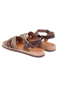 Braune Leder-Sandalen mit geflochtenen Akzenten, die mehrere Riemen und einen Schnallenverschluss aufweisen. Flache Sohle mit einem leichten Plattformdesign.