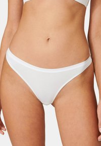 Weißer Baumwoll-Thong mit glatter Textur, ausgestattet mit einem dünnen elastischen Bund. Minimalistisches Design, keine Muster oder sichtbaren Hardware-Details.