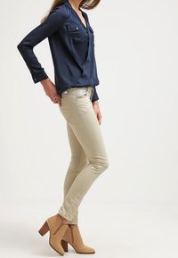Marinblus med lång ärm och två bröstfickor, i kombination med tanfärgade skinny jeans och beige ankelboots med klack. Släta tyger och figurnära design.