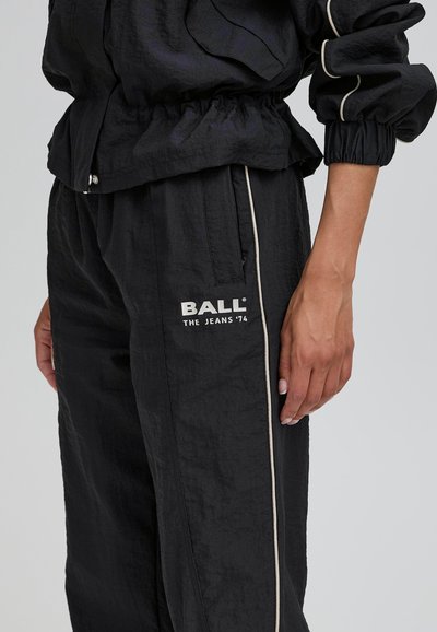 Schwarze leichte Jacke mit elastischen Bündchen und Saum, kombiniert mit passenden Hosen mit Seitenstreifen und dem weißen Logo "BALL". Strukturierter Stoff.