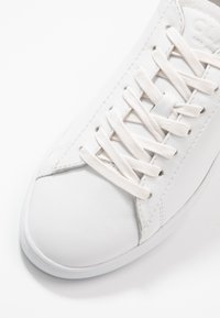 Baskets en cuir blanc avec des lacets blancs assortis noués en motif croisé, vues de dessus en se concentrant sur la zone arrondie des orteils.