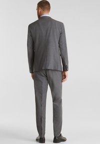 Completo grigio con texture liscia, giacca a un bottone e pantaloni dritti. Scarpe nere completano l'outfit.