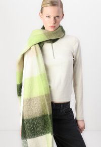 Rectangular wool scarf featuring a green, beige, and white striped pattern. Soft texture and slightly fuzzy surface.