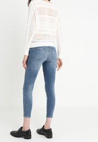 Suéter blanco de punto texturizado y de gran tamaño con un patrón de rayas. Se lleva con jeans ajustados de color azul claro y zapatos negros con cordones.