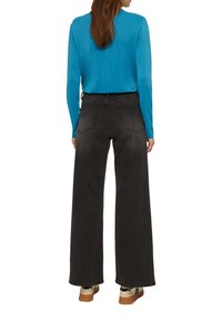 Schwarze weite Jeans mit hoher Taille, mit Ausbleichungen und Gesäßtaschen. Kombiniert mit einem blauen Langarmoberteil und hellen Sneakers.