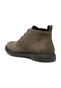 Botas de ante marrón hasta el tobillo con punta redondeada, suela plana de goma negra y cordones oscuros. Presenta una tira en la parte posterior para facilitar su uso.