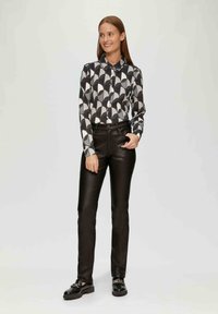 Koszula z długim rękawem w geometryczny wzór w kolorach czarnym, białym i szarym, w połączeniu z czarnymi spodniami z ekoskóry oraz czarnymi butami.