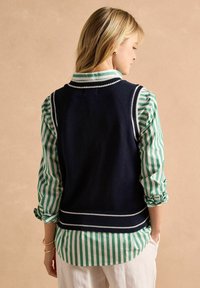 Tumesinise kudumvesti valgete äärtega kantakse rohelise ja valge triibulise särk üle. Disain sisaldab varrukatuks ja soonikuid.