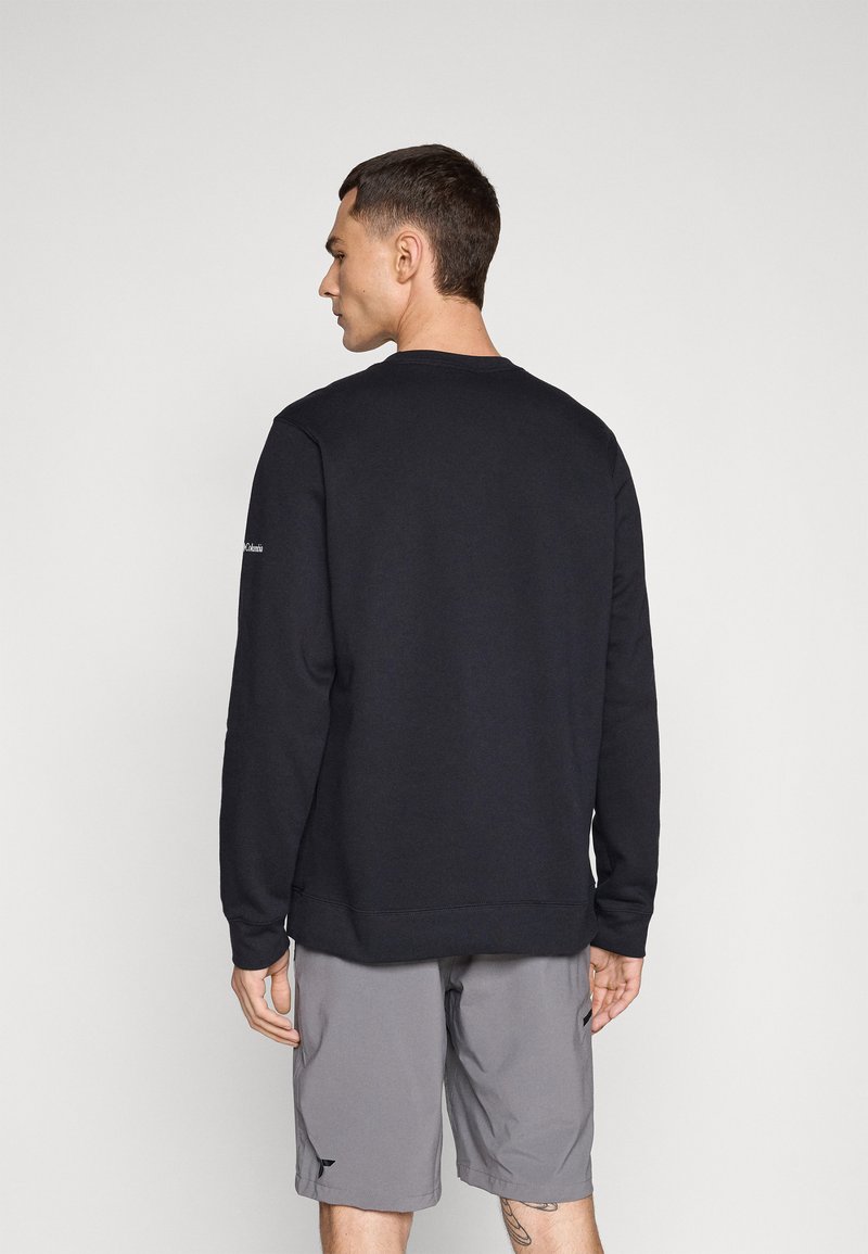 Sweatshirt noir à col rond et manches longues, en matériau doux, associé à un short gris, vu de dos.