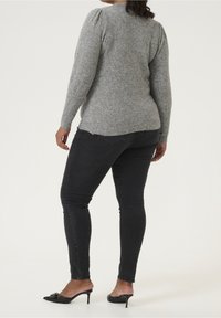 Grauer gestrickter Pullover mit engen Ärmeln und strukturierter Oberfläche. Kombiniert mit schwarzen Skinny-Jeans und schwarzen High-Heel-Mules mit dekorativen Akzenten.
