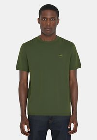 Maglietta verde a maniche corte con collo rotondo, realizzata in tessuto morbido, con un piccolo logo giallo sul petto e un design semplice.