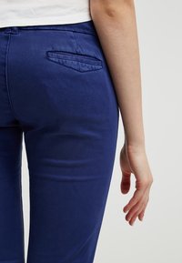 Marineblå åtsittande byxor i bomullsblandning, med en enkel bakficka som har en diskret snedslå och en slät yta.