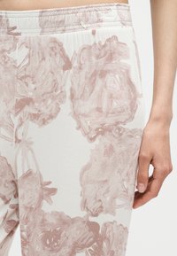 Gros plan du bas du torse et du bras d'une personne portant un pantalon clair avec un motif floral abstrait rose doux et une taille élastique.