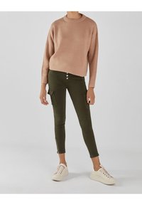 Stickad rosa tröja med rund halsringning, tillsammans med olivgröna cargobyxor med knappar och sidoglidlås, bärs med vita sneakers.