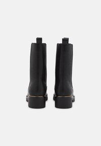 Botas de tobillo de cuero negro con un diseño elegante, que presentan un tubo recto, tiradores y una suela gruesa y texturizada con un acento dorado.