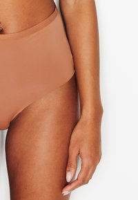 Culotte de bikini taille haute, sans coutures, de couleur beige clair, fabriquée en tissu lisse et extensible. Dispose d'une ceinture douce et d'un design minimaliste.