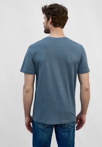 Korte mouwen, ronde hals t-shirt in gedempt blauwe stof. Zachte textuur met een lichte glans, achterkant toont schone lijnen en een ontspannen pasvorm.