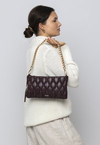 Gestepptes burgunderfarbenes Handtasche mit einem goldenen Kettenriemen, mit einer glatten Ledertextur und einem goldenen Logo-Detail.