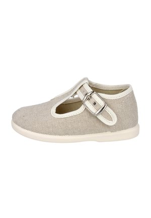 Zapato para niño pequeño de tela beige claro con correa en T y hebilla plateada, ribete blanco y suela de goma, mostrado de lado sobre un fondo blanco.