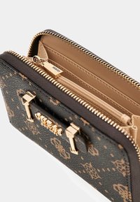Portafoglio a motivo marrone scuro con zip in tonalità oro e logo Guess, parzialmente aperto che mostra l'interno beige e un compartimento per le monete con zip.