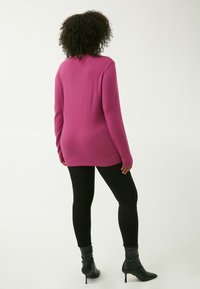 Maglione a maglia magenta con maniche lunghe, polsini e orlo a costine, indossato sopra leggings neri e abbinato a stivali neri con tacco, visto da dietro.