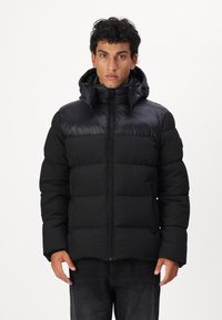 Giubbotto puffa nero con colletto alto, imbottitura orizzontale e zip frontale. Include un cappuccio staccabile e tasche laterali.