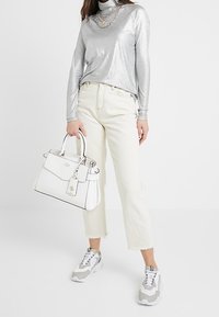 Hopeinen, pitkähiainen paita; valkoinen käsilaukku, jossa on hintalappu; vaaleat, lyhennetyt farkut; harmaavalkoiset lenkkarit; sileät pinnat; tyylikäs muotoilu.