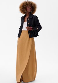 Czarna krótka kurtka z dużymi guzikami, biała teksturowana bluzka i beżowa, zwiewna spódnica maxi. Warte uwagi cechy to szerokie rękawy i drapowany krój.