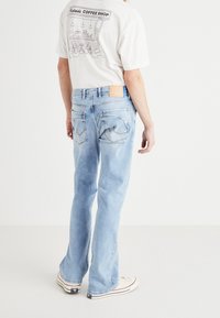 Jeans de mezclilla azul claro con un ajuste relajado, que cuentan con bolsillos traseros y una etiqueta de cuero marrón. Combinados con una camiseta gráfica blanca.