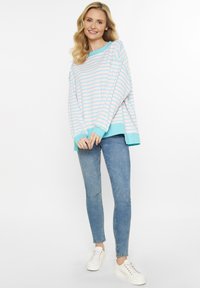 Camicetta a maniche lunghe a righe blu e bianche con dettagli turchesi, abbinata a jeans skinny blu chiaro e sneakers bianche.